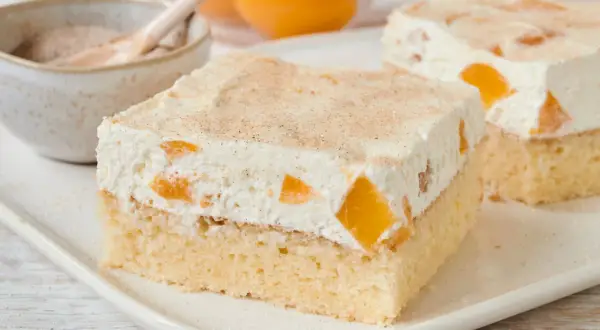 Saftiger Pfirsich Schmand Kuchen mit Zimt bestreut, serviert auf einem weißen Teller.