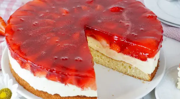 Ein saftiger Erdbeerkuchen mit Vanillepudding und einer glänzenden Erdbeer-Gelee-Schicht. Ein Stück ist bereits herausgeschnitten.
