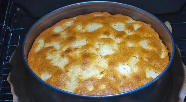 Ein goldbrauner, versunkener Apfelkuchen bäckt in einer runden Form im Ofen. Die Äpfel sind im Teig versunken und bilden ein schönes Muster.