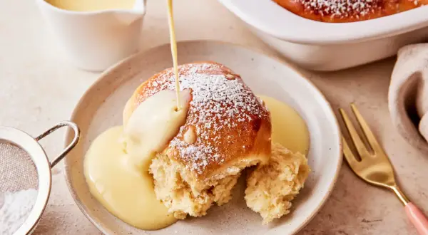 Ein Buchtel wird mit Vanillesauce übergossen, bestäubt mit Puderzucker. Ein köstliches Buchteln Rezept zum Genießen.