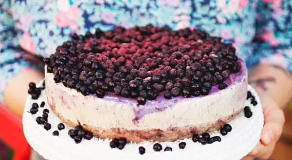Ein köstlicher Blueberry Cheesecake, üppig belegt mit frischen Blaubeeren, wird auf einem weißen Tortenständer präsentiert.
