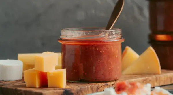 Glas mit rotem Chutney, daneben Käsewürfel und -stücke. Perfekt für leckere Chutneys Rezepte.