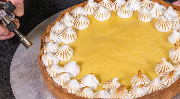Ein köstlicher Lemon Curd Kuchen mit Baiserhauben wird mit einem Brenner karamellisiert.
