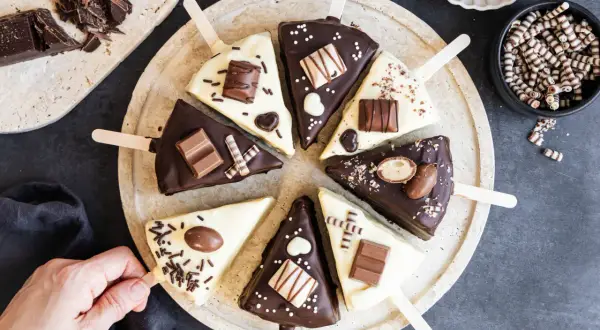 Schokoladige Cheesecake-Sticks, verziert mit Schokoriegeln und Streuseln, auf einem Teller arrangiert.