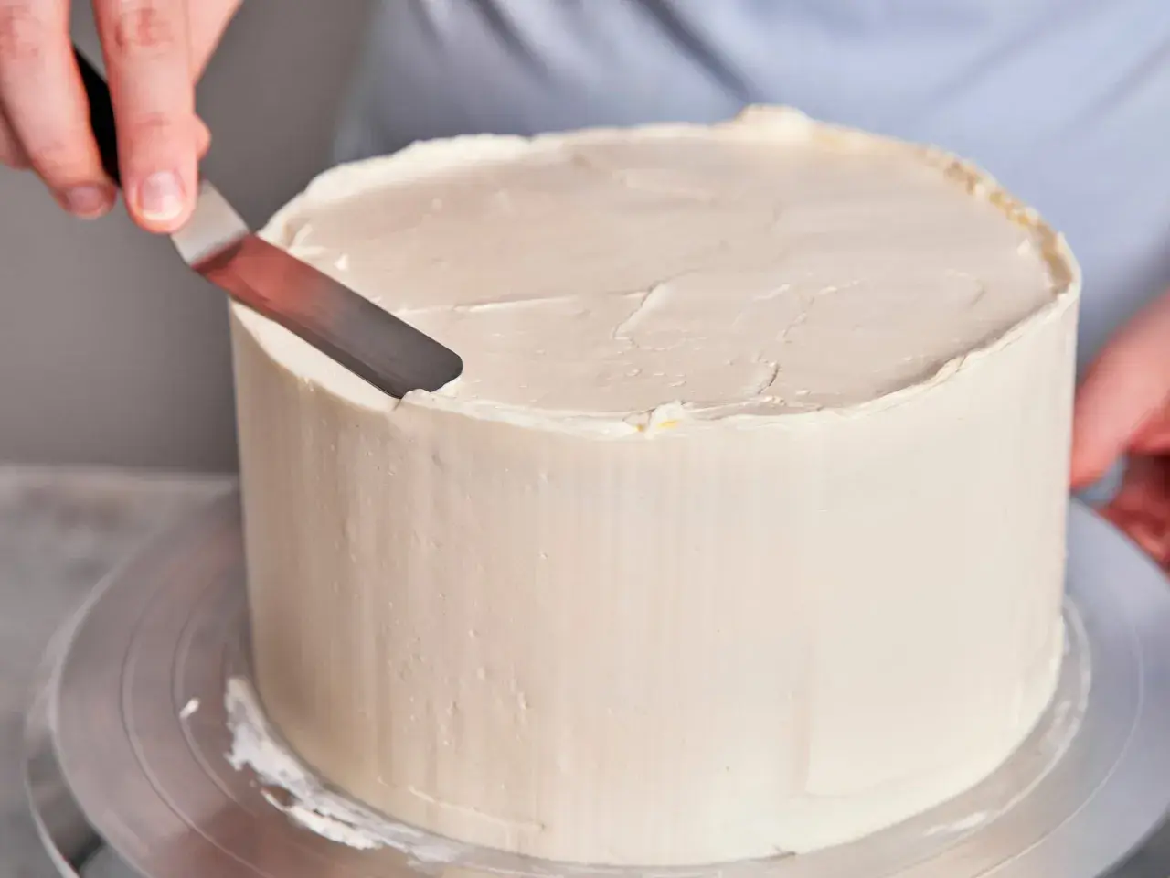 Eine Hand glättet mit einem Spatel die cremige Buttercreme-Torte.
