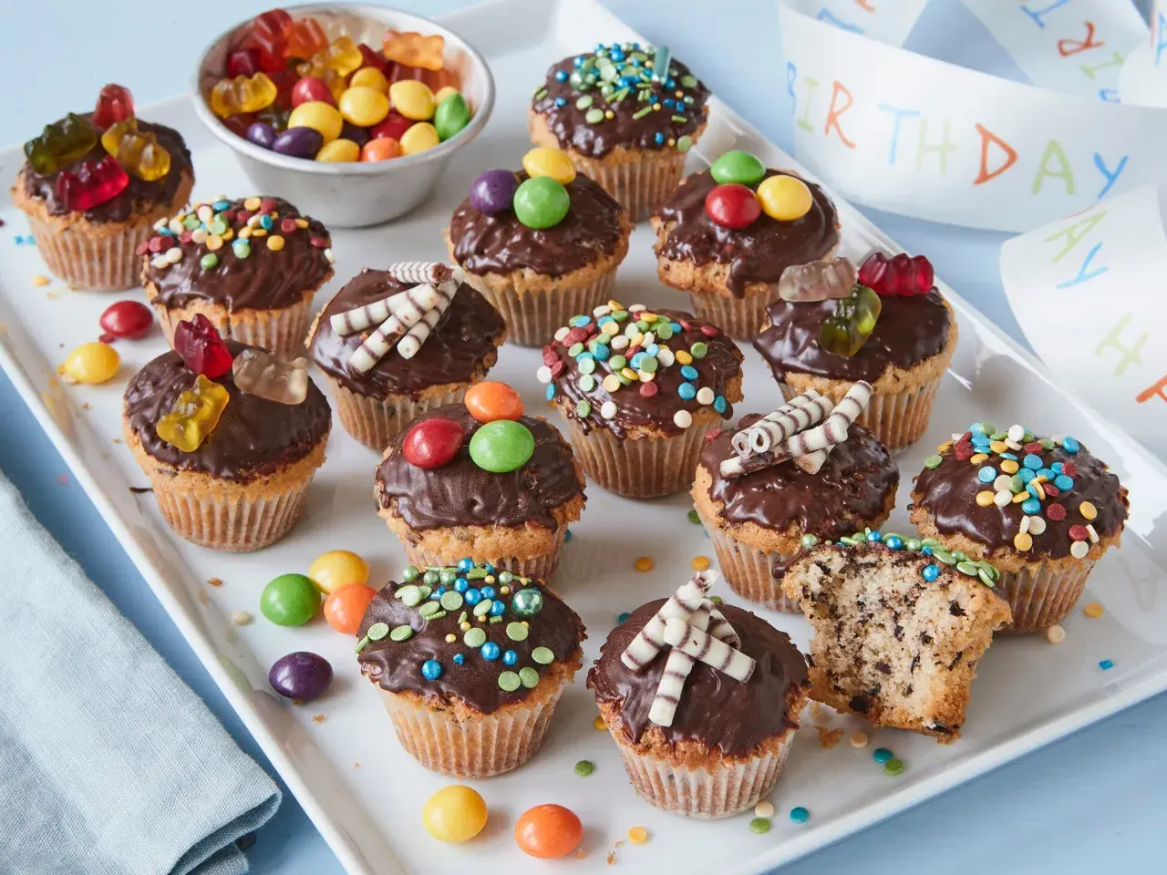 Bunte Muffins mit Schokoglasur und Gummibärchen, perfekt für einen Kindergeburtstag.