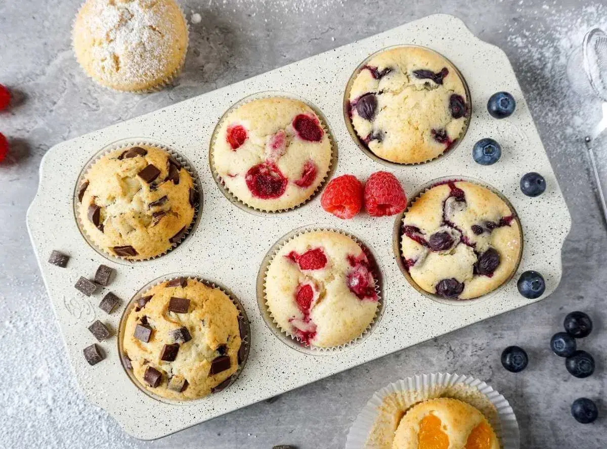 Leckeres Muffins Rezept: Schoko-, Himbeer- und Blaubeermuffins in einer Form, daneben frische Beeren und Schokostückchen.