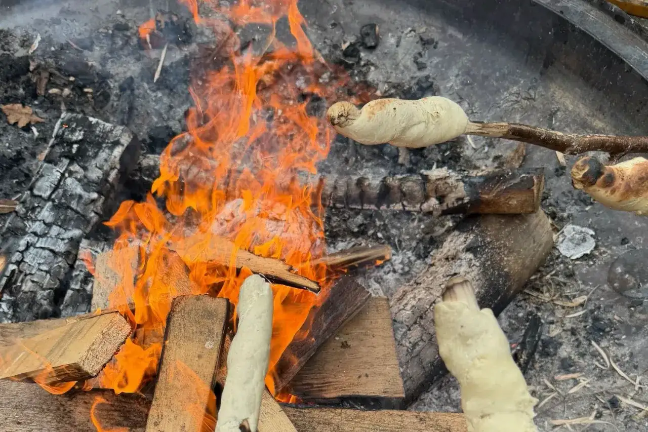 Stockbrot rezept: Teig wird über offenem Feuer gebacken. Flammen lodern, Holz glüht.