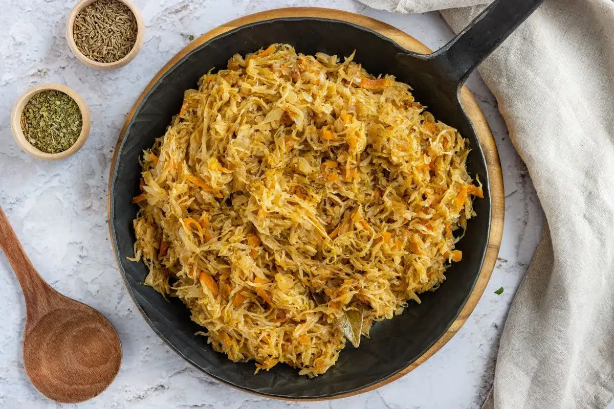 Herzhaftes Sauerkraut im Topf, bereit für ein köstliches Sauerkraut Rezept. Daneben Kümmel und Kräuter.