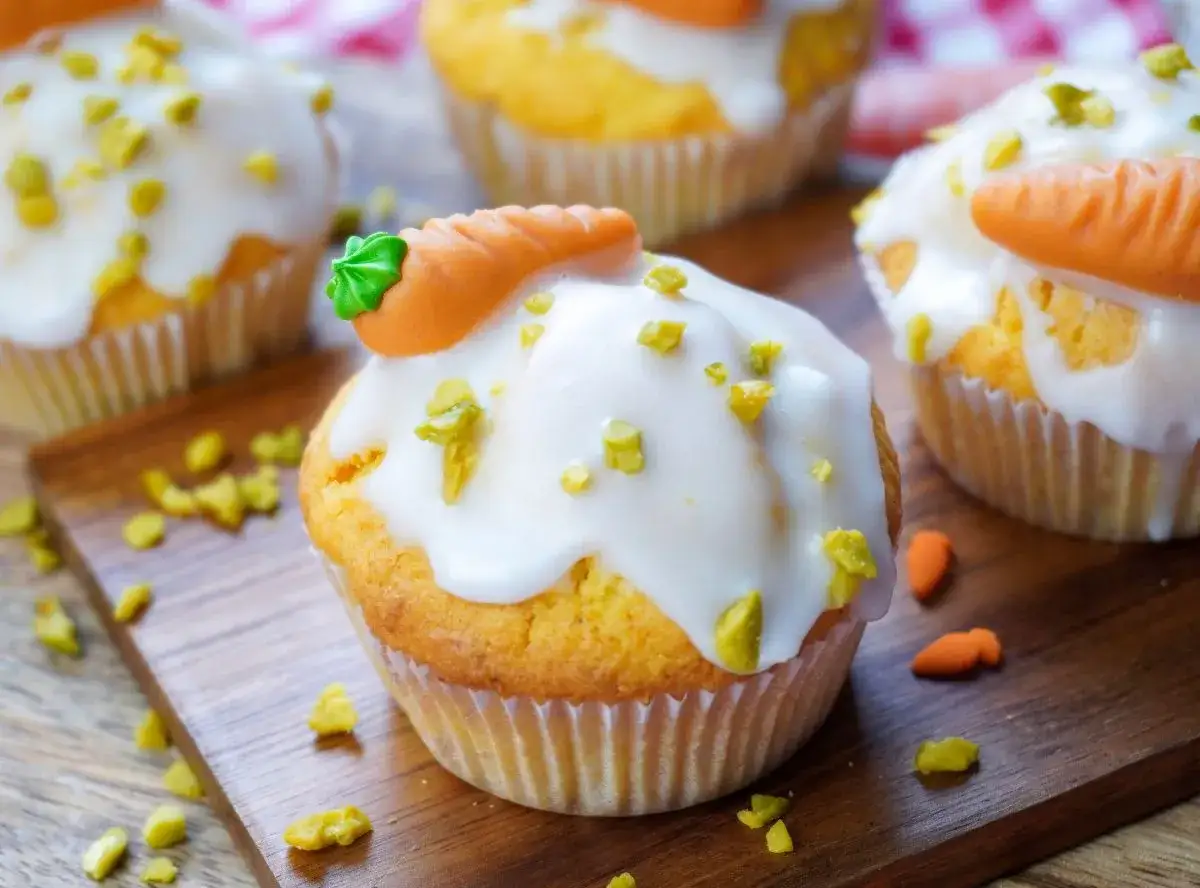 Leckere Karotten Muffins mit weißer Glasur und kleinen Marzipan-Karotten verziert.