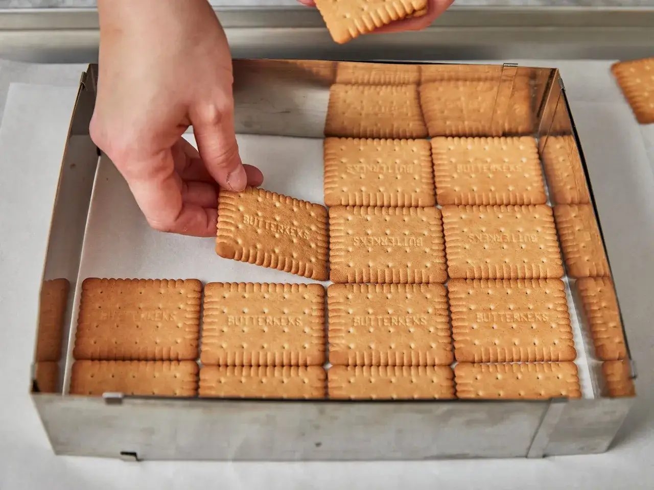 Hände legen Butterkekse in eine Form für einen Butterkeks Kuchen.