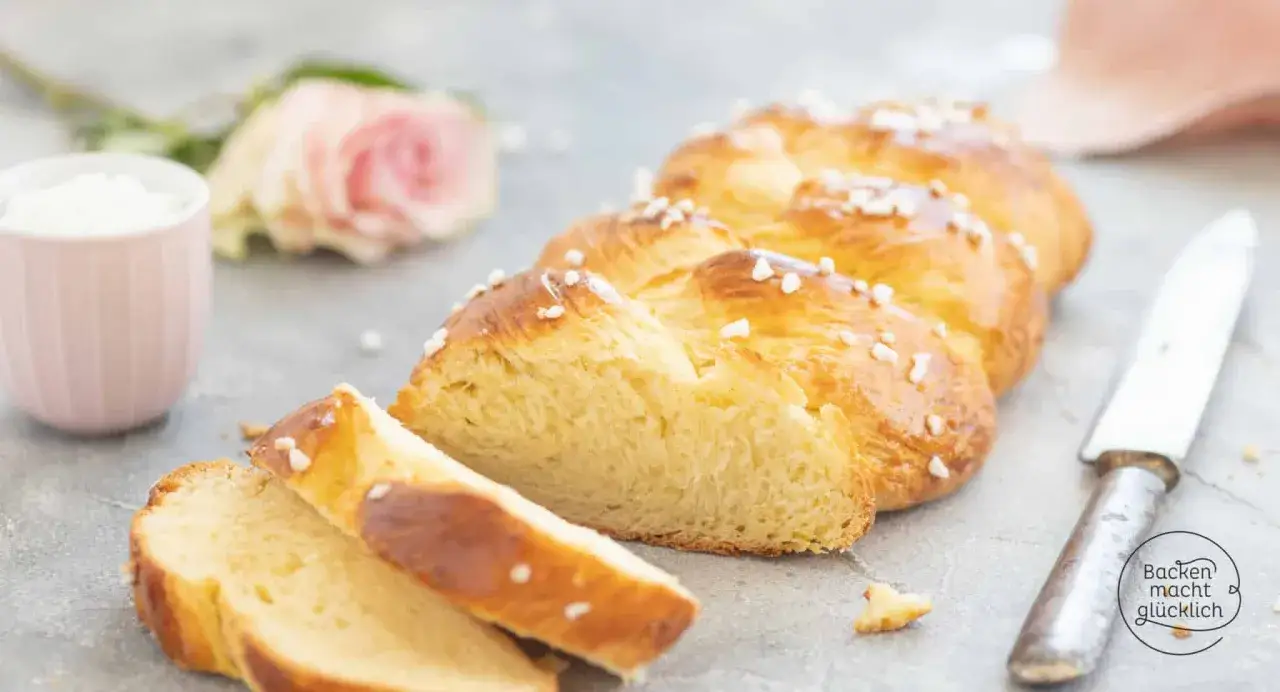 Ein goldbrauner Hefezopf, bestreut mit Hagelzucker, liegt angeschnitten auf grauem Untergrund. Ein tolles Rezept für den Hefezopf!