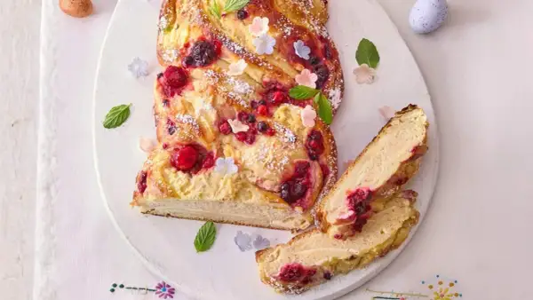 Ein köstlicher Osterzopf mit Quark und Beeren, bestäubt mit Puderzucker und verziert mit Minze und kleinen Blüten.