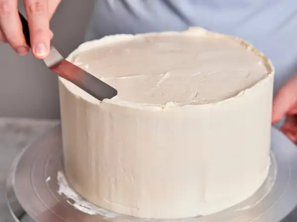 Eine Hand glättet mit einem Spatel die cremige Buttercreme-Torte.