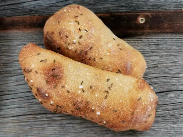Zwei frisch gebackene Seelen mit Kümmel und Salz auf rustikalem Holz.