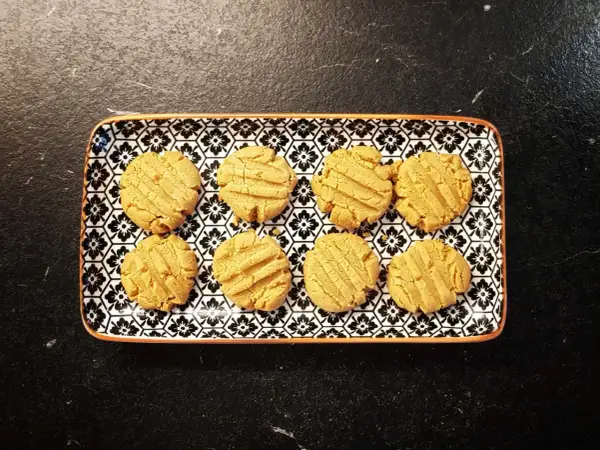 A rectangular plate with a black and white floral pattern holds eight golden-brown kekse ohne zucker.