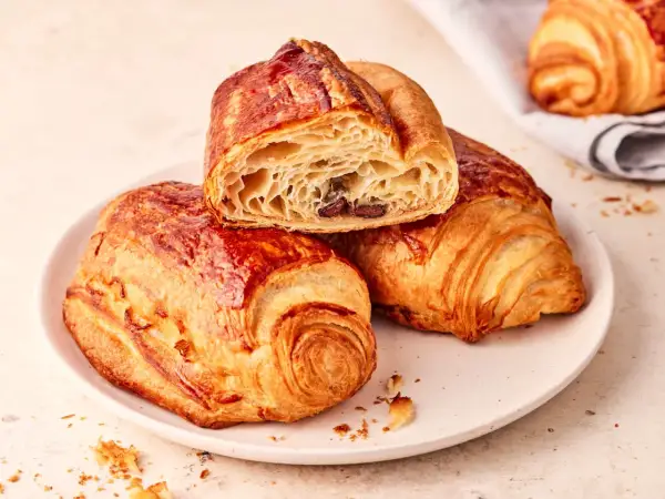 Zwei goldbraune, knusprige Pain au Chocolat auf einem Teller, eines davon angeschnitten, enthüllt die schokoladige Füllung.