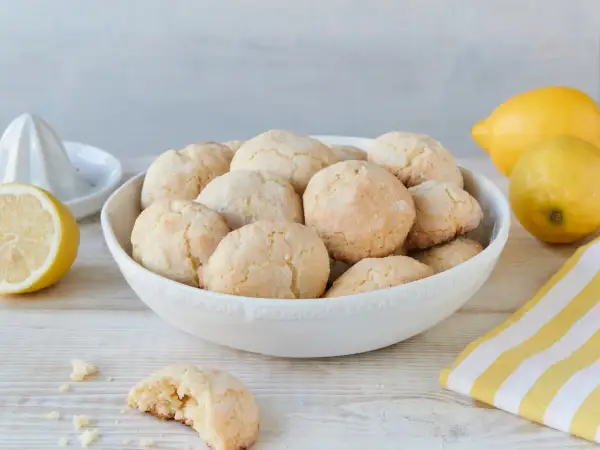 Schüssel voller zitronen cookies, daneben Zitronen und ein Zitronenpresse. Ein Cookie ist angebrochen.