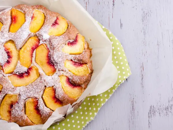 Saftiger Pfirsichkuchen, mit Puderzucker bestäubt, auf einem grünen Tupftuch. Ein Genuss für die Sinne!