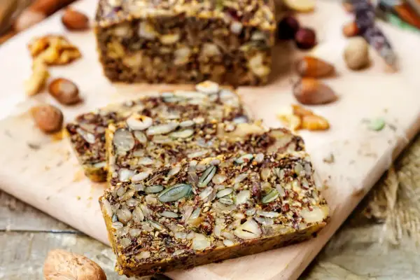 Slices of hearty keto brot, packed with seeds and nuts, rest on a wooden board.
