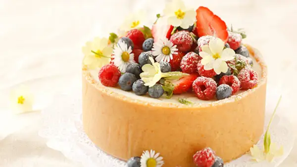Torte mit frischen Beeren und Blumen dekoriert.