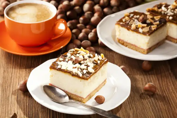 Ein Stück cremiger Käsekuchen mit Schokoladenglasur und Nüssen, dazu eine Tasse Kaffee. Perfekt für einen schnellen Kuchengenuss.