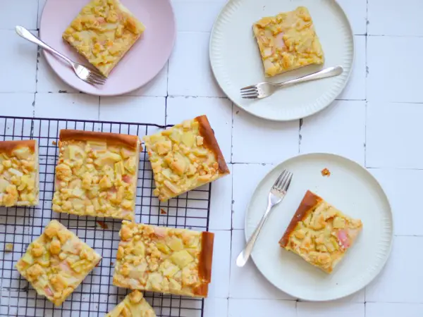 Saftiger Rhabarberkuchen auf Hefeteig mit Streuseln, auf Tellern und einem Kuchengitter arrangiert.