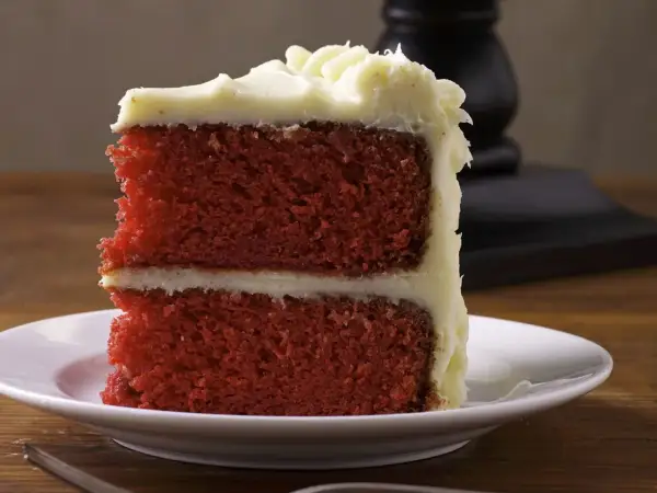 Ein Stück saftiger **red velvet** Kuchen mit cremiger Glasur auf einem weißen Teller.