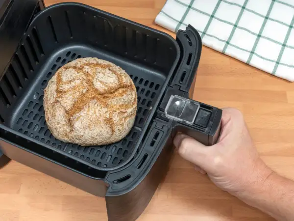 Ein goldbraunes Brot liegt im Korb eines Airfryers. Perfekt für schnelles brot backen im airfryer.