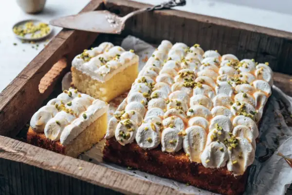 Ein köstlicher Joghurt Kuchen mit luftiger Creme und gehackten Pistazien, serviert auf einer rustikalen Holzschale.