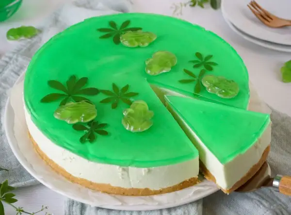 Grüne Philadelphia Torte Waldmeister mit Gummifröschen und Blättern verziert. Ein Stück wird gerade herausgeschnitten.