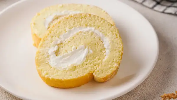 Zwei Scheiben einer saftigen Zitronenrolle mit cremiger Füllung auf einem weißen Teller. Ein köstliches Zitronenrolle Rezept zum Nachbacken.