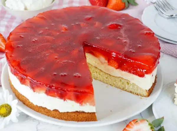 Ein saftiger Erdbeerkuchen mit Vanillepudding und einer glänzenden Erdbeer-Gelee-Schicht. Ein Stück ist bereits herausgeschnitten.