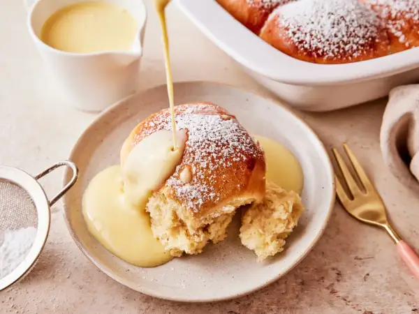 Ein Buchtel wird mit Vanillesauce übergossen, bestäubt mit Puderzucker. Ein köstliches Buchteln Rezept zum Genießen.