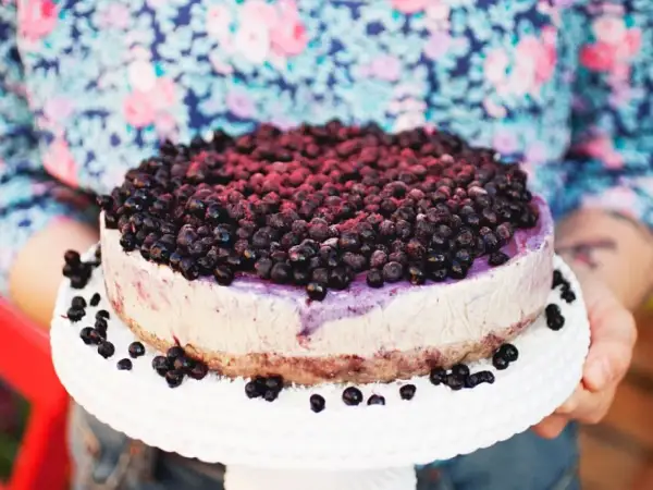 Ein köstlicher Blueberry Cheesecake, üppig belegt mit frischen Blaubeeren, wird auf einem weißen Tortenständer präsentiert.