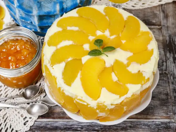Eine köstliche Pfirsich Maracuja Torte, dekoriert mit frischen Pfirsichspalten und Minze. Daneben ein Glas Pfirsichmarmelade.
