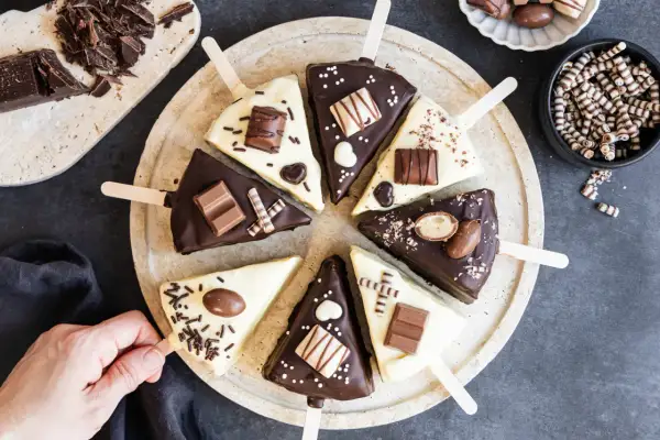 Schokoladige Cheesecake-Sticks, verziert mit Schokoriegeln und Streuseln, auf einem Teller arrangiert.
